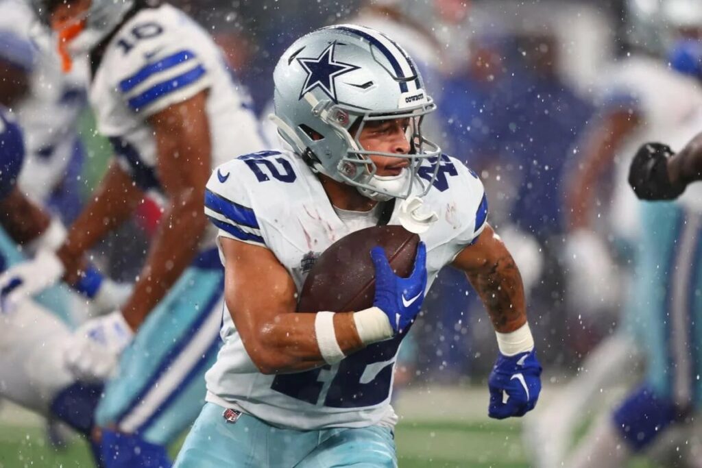 Cowboys' Deuce Vaughn, dressed in a white and blue uniform, sprints with the ball during a game.