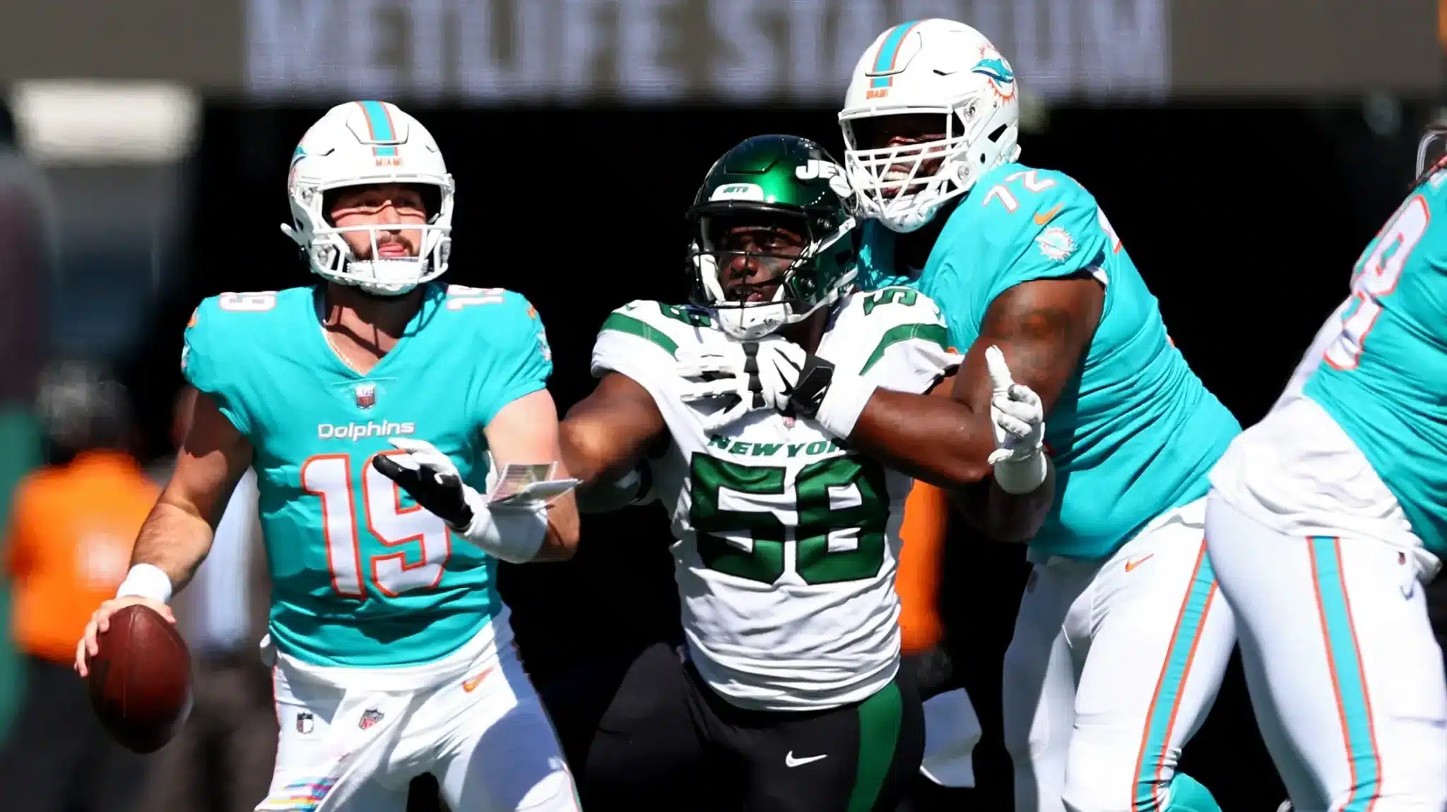 Football players from the Miami Dolphins and New York Jets in action during a game, with a player preparing to throw a pass.