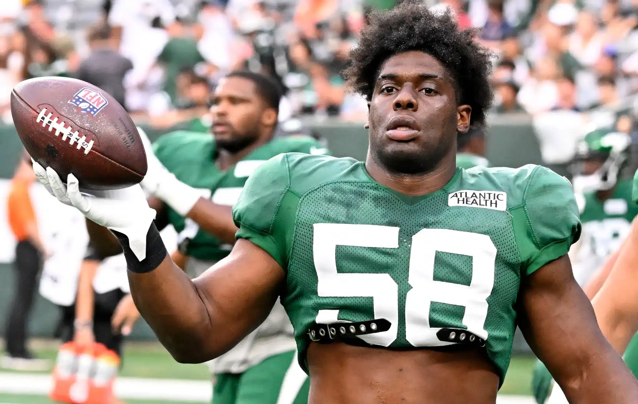 Football player in a green jersey holding a football while gesturing to the camera during a game.