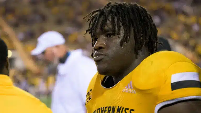 A football player in a yellow "Southern Miss" jersey stands on the sidelines during a game.