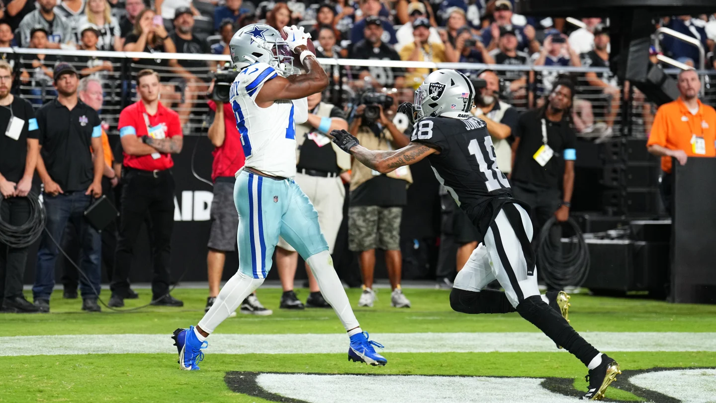 Dallas Cowboys player catching a football while being defended by a Las Vegas Raiders player during a game.