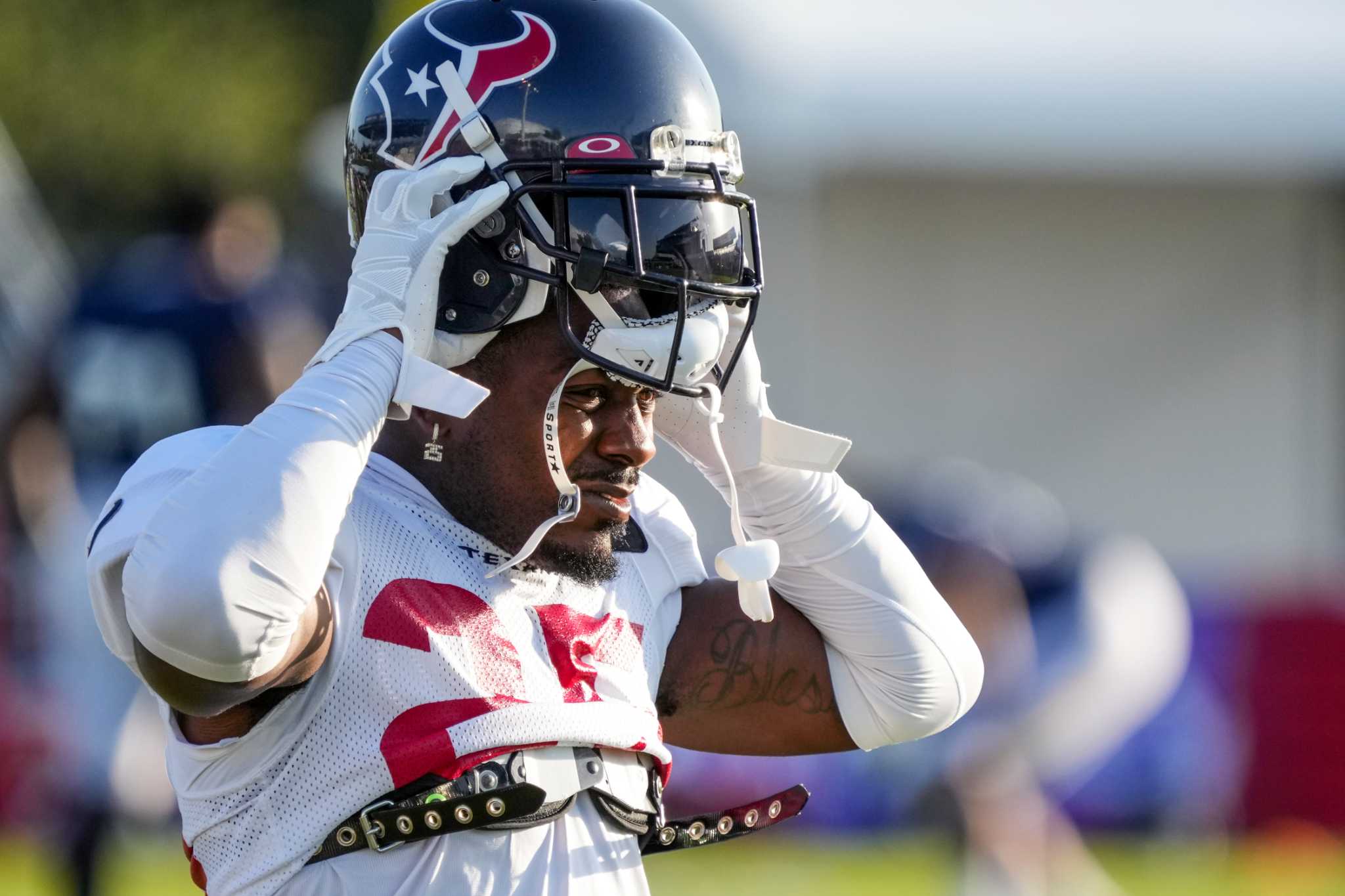 A football player in Houston Texans gear adjusts his helmet during practice.