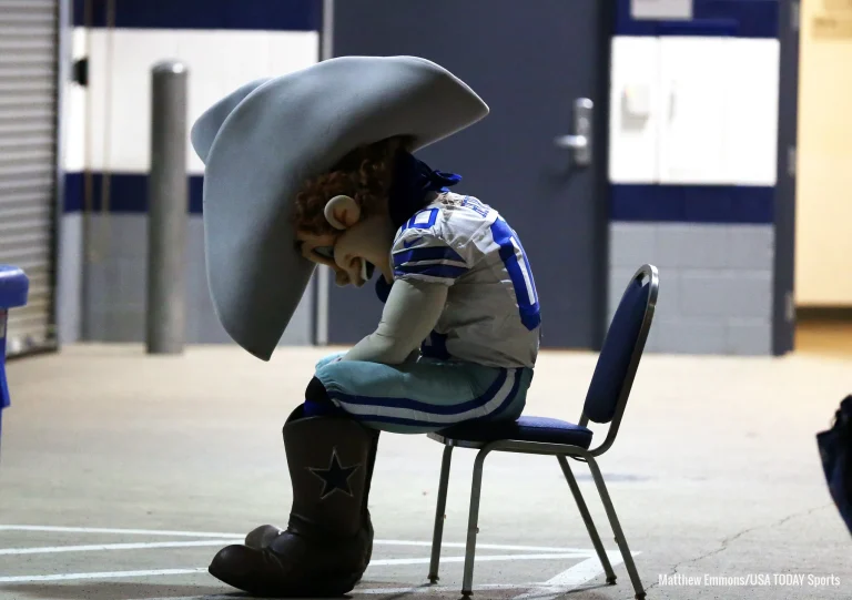 A sports mascot in cowboy attire sits on a chair with a slumped posture in a hallway.