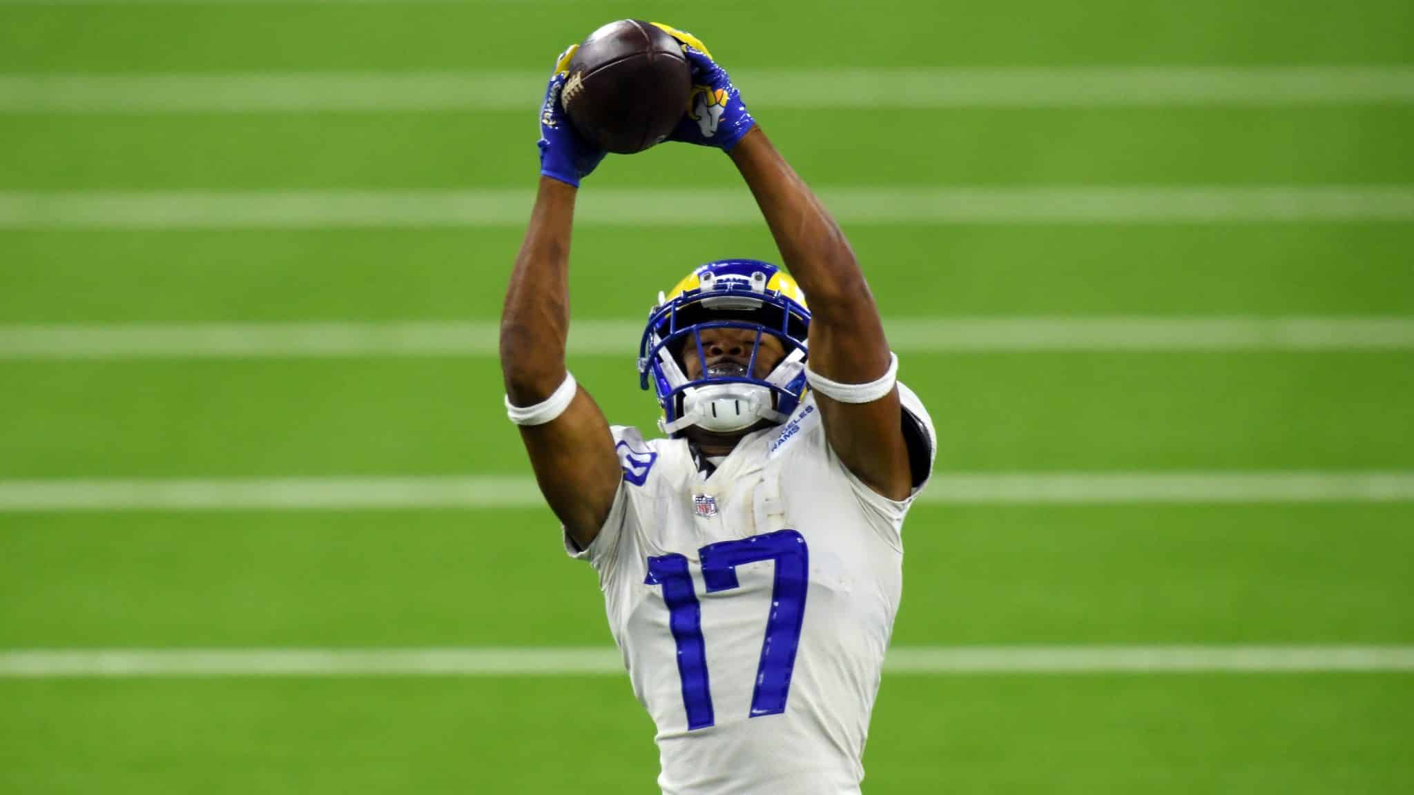 Football player in a white and blue uniform catches the ball with both hands raised above his head on the field.