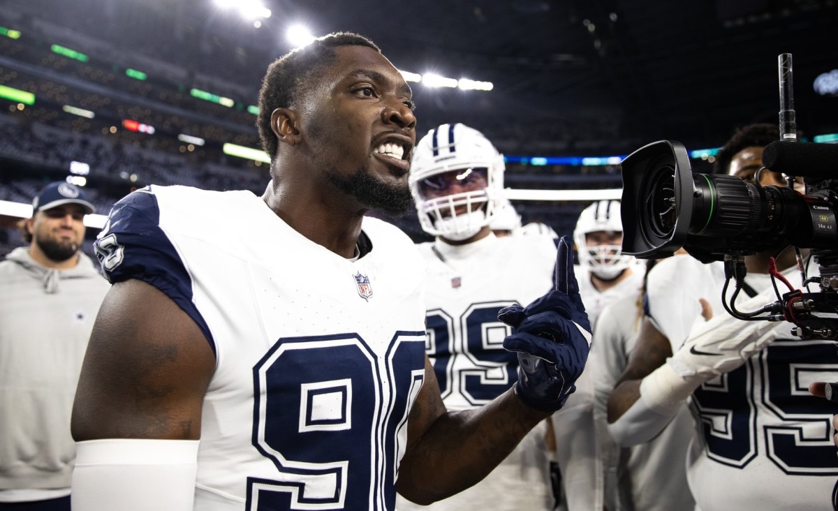 Football player in a white uniform gestures while speaking passionately towards a camera on the sidelines of a stadium.