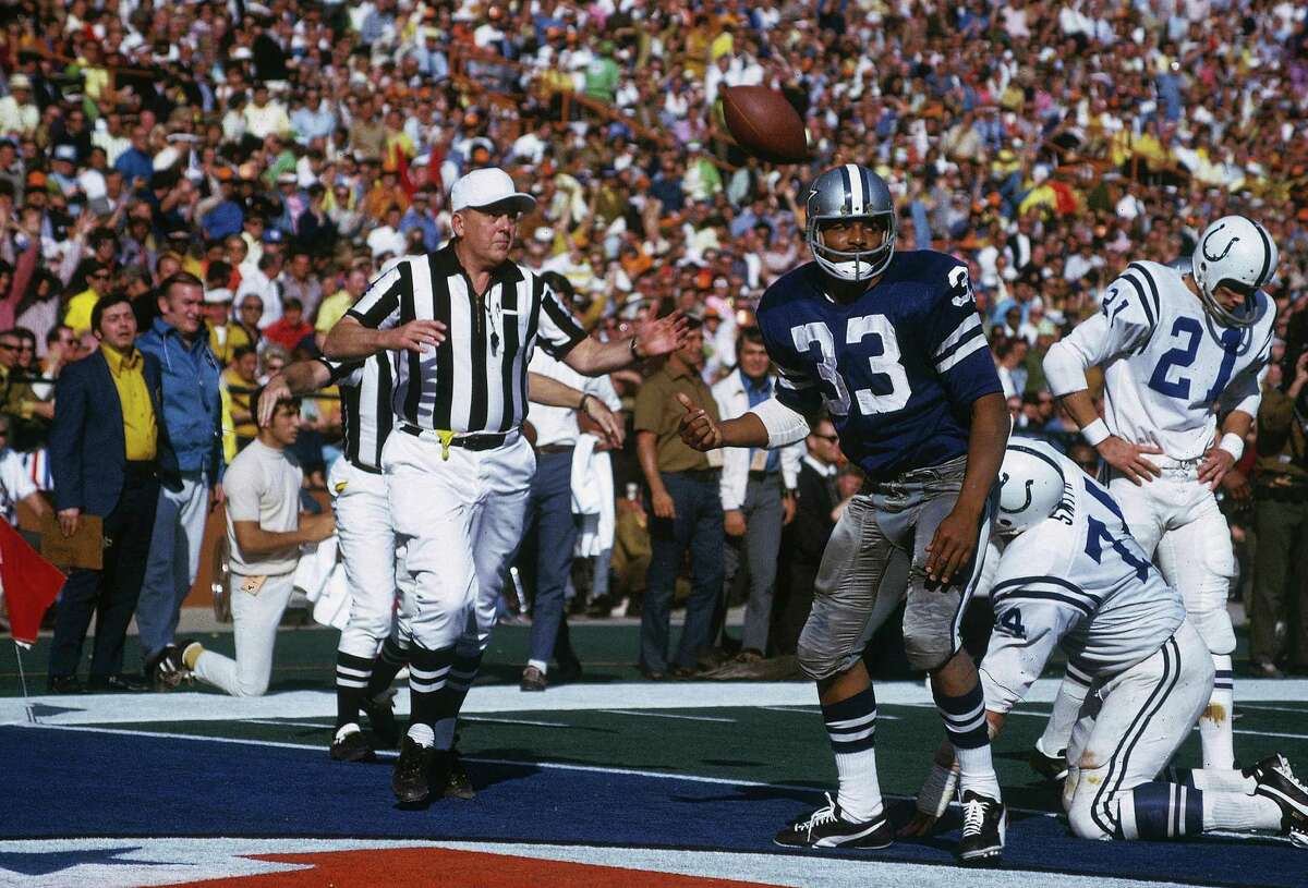 Football player in a blue jersey celebrates a touchdown while a referee signals the score and another player kneels nearby.