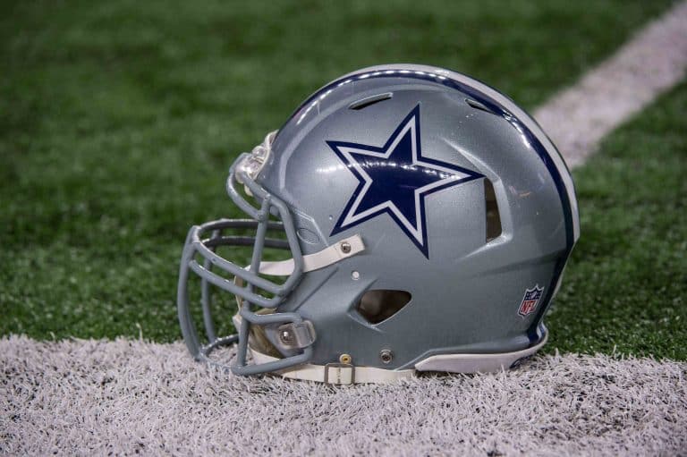 Silver football helmet with a blue star logo, placed on a field with artificial turf.