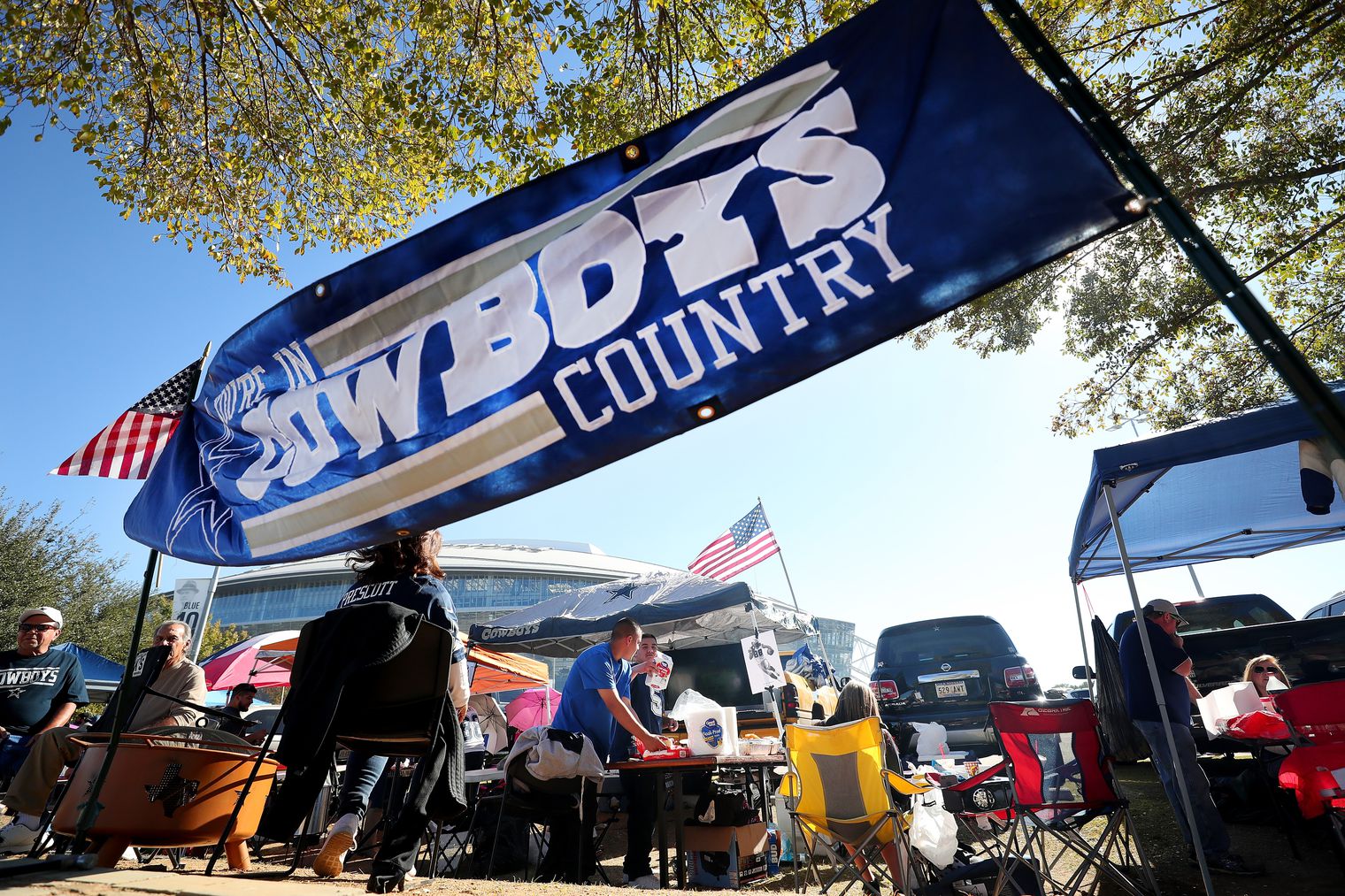 A group of people tailgating under a "Cowboys Country" banner with chairs, food, and American flags in the background.