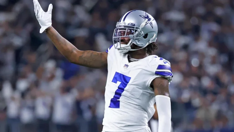 Football player wearing a white and blue Dallas Cowboys uniform with the number 7 raises his left arm during a game.