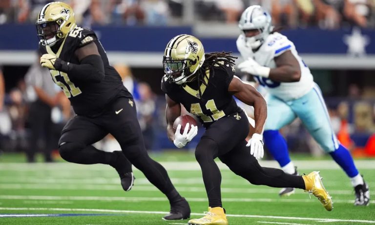 Football players from two teams in action on the field, one holding a football and running with teammates nearby.